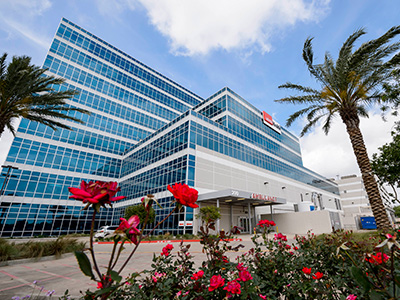 UTMB Clear Lake Campus Exterior of UTMB Clear Lake campus with glass windows, palm trees and rose gardens.