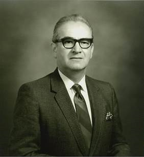 Black‑and‑white studio portrait of Dr. Hector Garcia wearing a suit jacket, dress shirt, tie, and glasses against a neutral background.